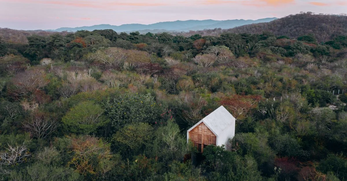Una serena toma aérea de una casa rodeada de árboles frondosos y colinas onduladas al anochecer, capturando la belleza natural.