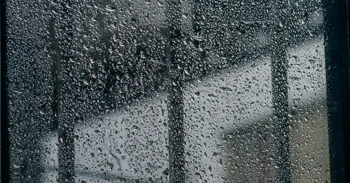 Primer plano de una ventana empapada de lluvia con gotas de agua, creando una atmósfera melancólica y fresca.