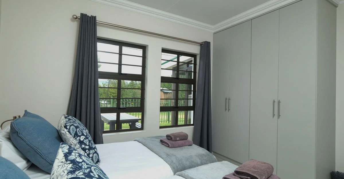Dormitorio contemporáneo con ropa de cama ordenada y vista al jardín.