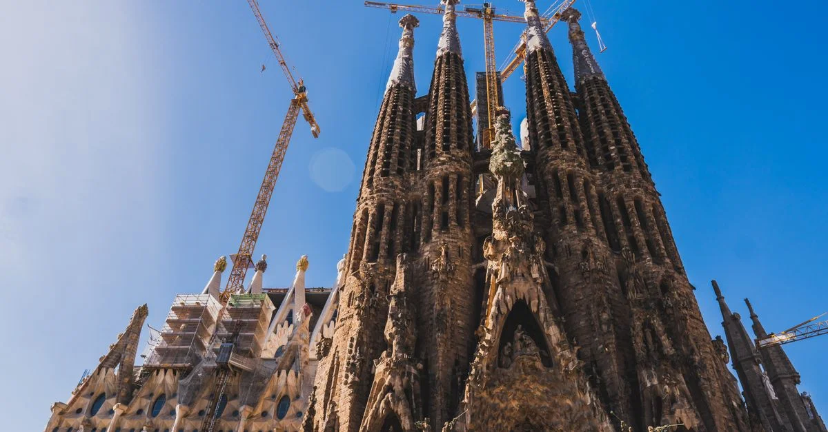 Vista de la intrincada fachada de la Sagrada Familia y grúas contra un cielo azul claro en Barcelona.