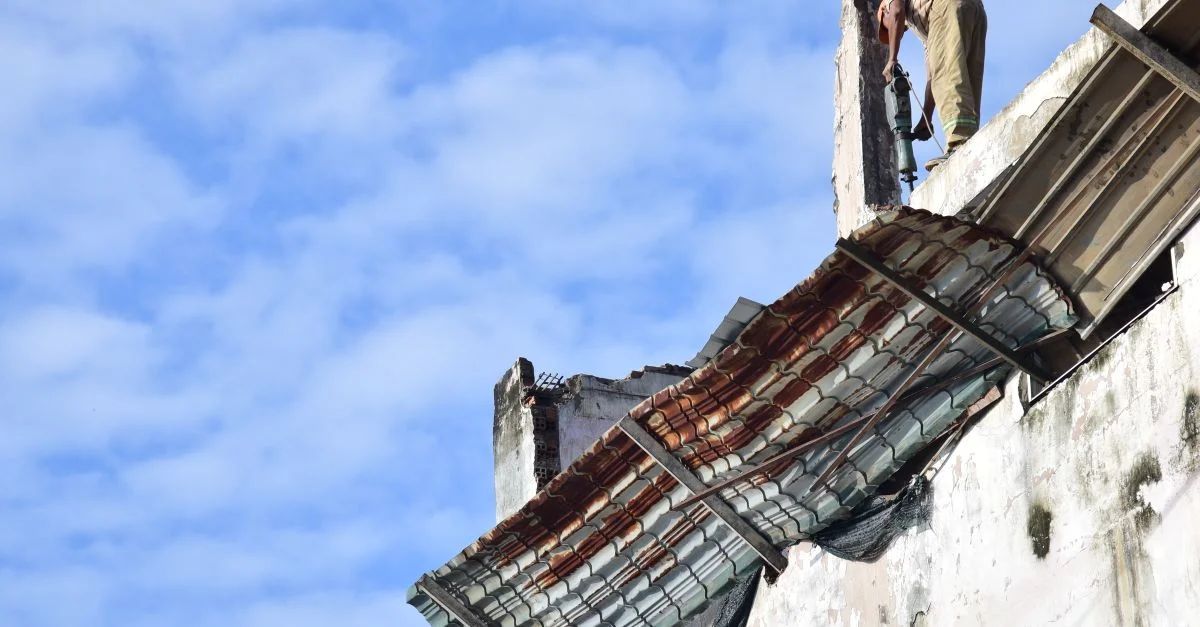 Un trabajador de la construcción repara un tejado en un edificio alto bajo un brillante cielo azul.