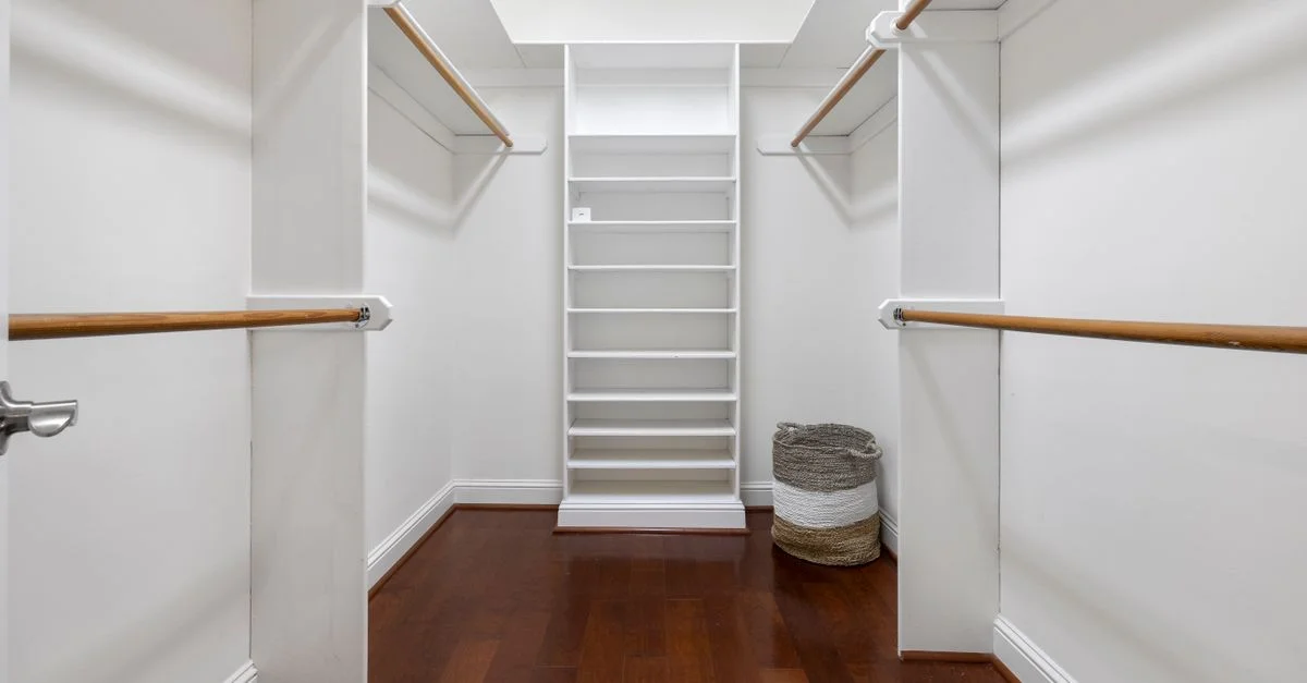 Armario walk-in vacío y minimalista con suelos de madera, estantes y barras para colgar.