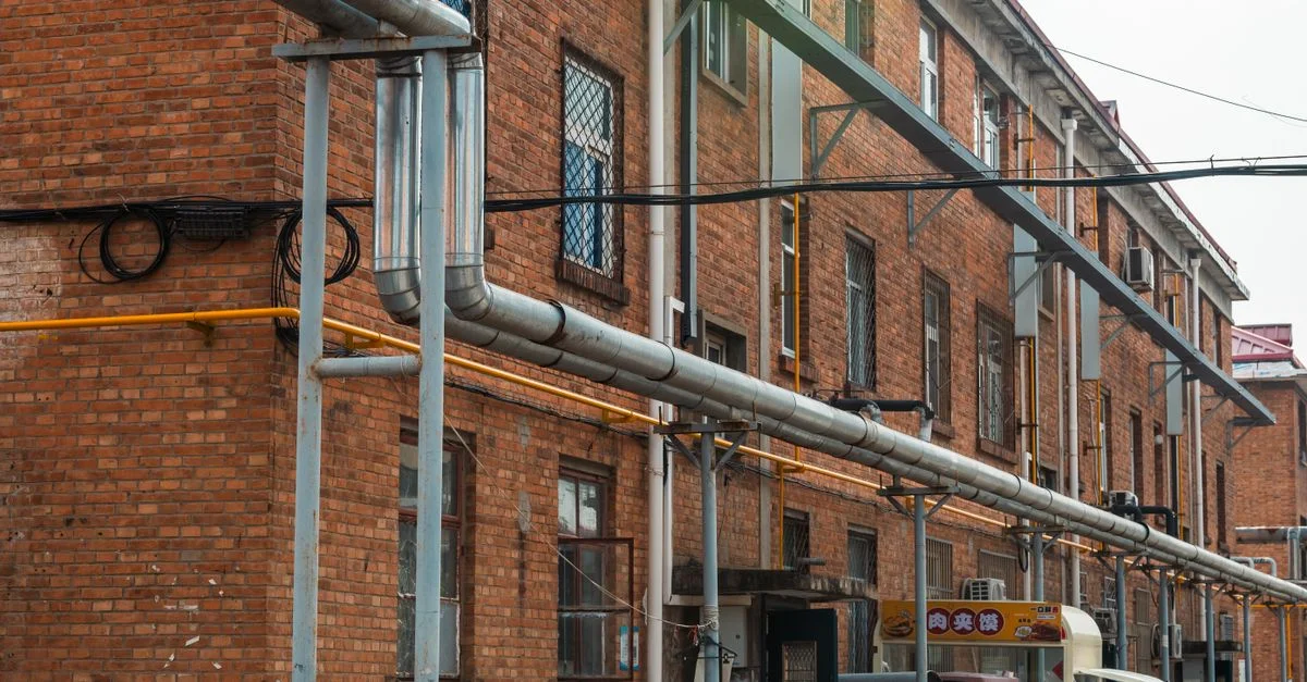 Vista exterior de edificio de ladrillo con tuberías industriales y líneas de servicios públicos expuestas.