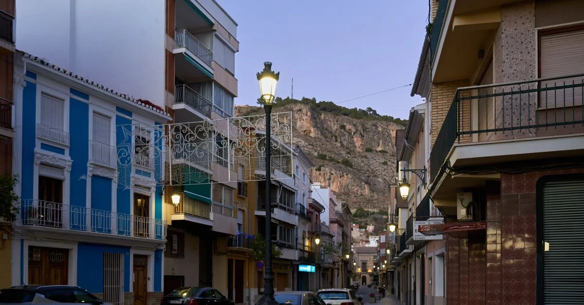Encantadora vista de una calle urbana con coches, edificios y una montaña al fondo al anochecer.