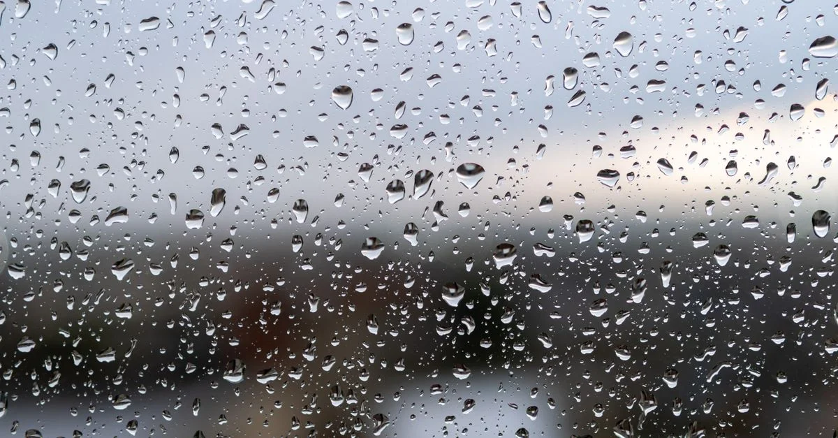 Una vista en primer plano de gotas de lluvia en el cristal de la ventana con un paisaje borroso de fondo.
